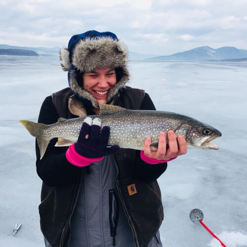 Excited woman holding lake trout while ice fishing